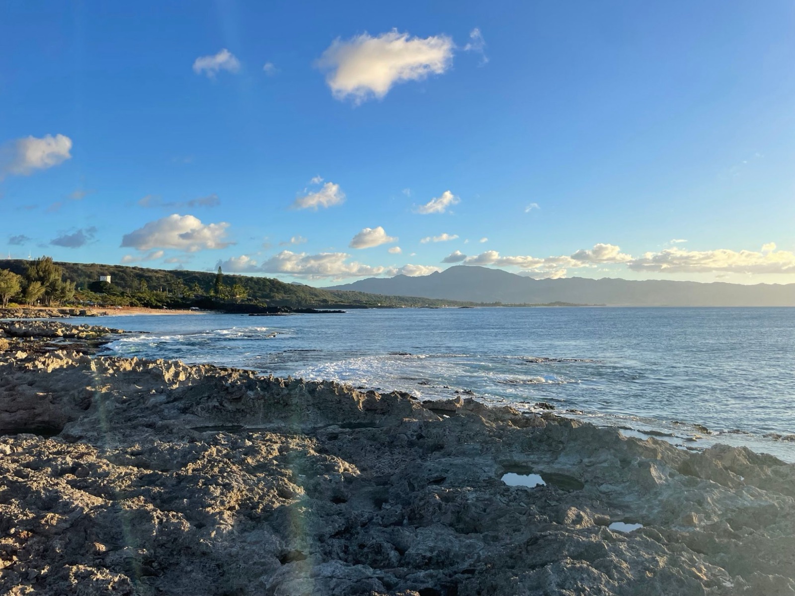 Rocky coastline at golden hour with mountains across the bay